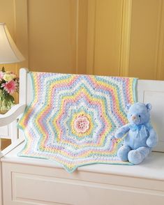 a teddy bear sitting on a bench next to a crocheted blanket that is shaped like a flower