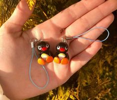 two small black and orange birds are hanging from earwires on a string in the palm of someone's hand