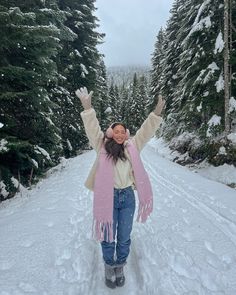 a woman standing in the middle of a snow covered road with her arms outstretched up