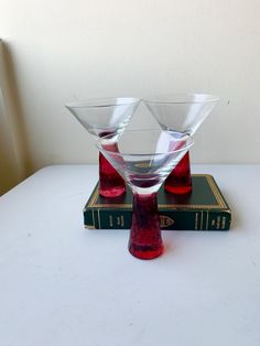 two wine glasses sitting on top of a book with red liquid in the bottom and inside