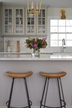 two stools are in front of the kitchen island with flowers on it and lights above