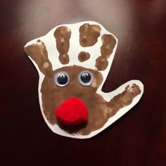 a handprinted christmas ornament with a red nose on a wooden table