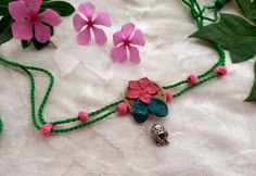 the necklace is decorated with flowers and beads on a table next to some green leaves