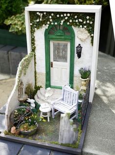 a miniature house with a white door and green trimmings on the front porch