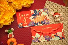 two red envelopes sitting on top of a table next to flowers and an orange toy