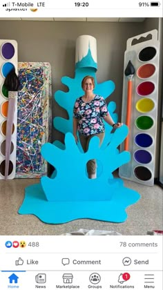 a woman sitting on top of a blue paper tree with paintbrushes in the background