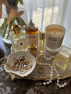 an assortment of perfumes and jewelry on a tray next to a vase with flowers