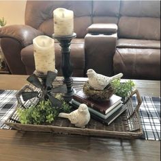 a tray with candles, books and birds on it in front of a leather couch