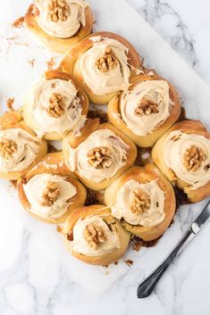 a white plate topped with rolls covered in cream cheese frosting and walnut toppings