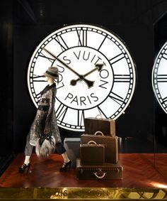 a woman walking past two large clocks on display