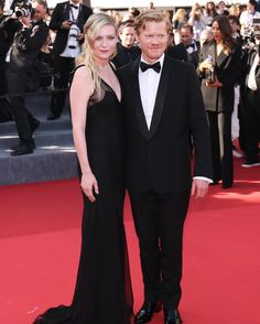 a woman in a black dress and a man in a tuxedo pose on the red carpet