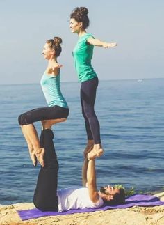 two women doing yoga on the beach with their feet in the air and one standing up