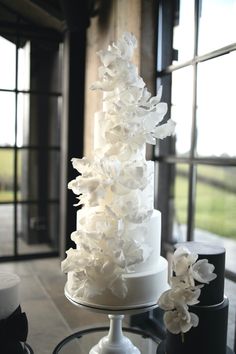 a wedding cake with white flowers on top is sitting on a table in front of a window