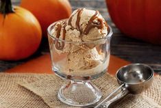 two scoops of ice cream in a glass bowl with spoon next to pumpkins