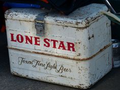 an old lunch box sitting on the ground next to some beer cans and other items