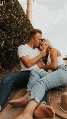 a man and woman sitting on the ground next to each other with their arms around each other