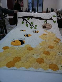 a quilt is being displayed on a table with people in the background looking at it