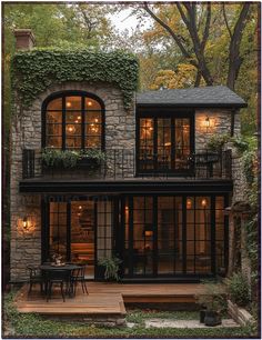 a stone house with lots of windows and plants on the balcony, surrounded by greenery