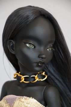 a doll with long black hair wearing a gold choker and chain around it's neck