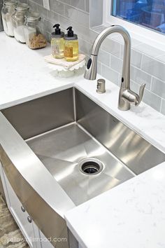 a stainless steel sink in a kitchen with marble counter tops and white subway backsplash