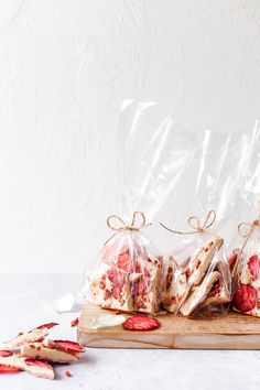 three bags of strawberry shortbreads sitting on top of a cutting board next to strawberries