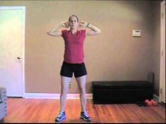 a woman standing in a living room with her hands behind her head