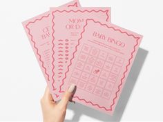 three pink baby shower game cards held up in the air by a woman's hand