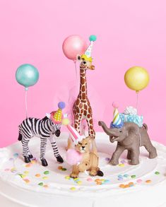 a birthday cake with animals and balloons on the top, in front of a pink background