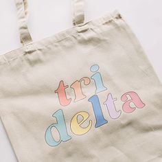 a canvas bag with the word tri delta printed on it, sitting on a white surface