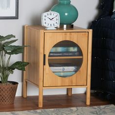 a small wooden cabinet with a clock on top next to a potted green plant