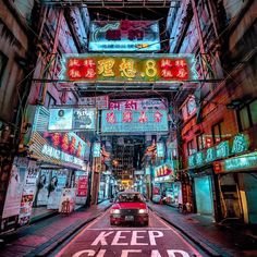 a red car driving down a street next to tall buildings with neon signs above it