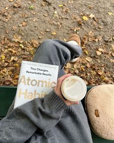 a person sitting on a bench holding a cup of coffee and a book in their hand