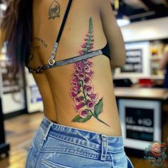 a woman with a flower tattoo on her back is wearing blue jeans and a black bra