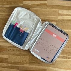 an open suitcase sitting on top of a wooden floor next to a pen and notebook