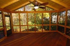 a screened porch with wood flooring and ceiling fan in the center, surrounded by trees