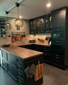 a kitchen with black cabinets and wooden counter tops, hanging lights above the sink area