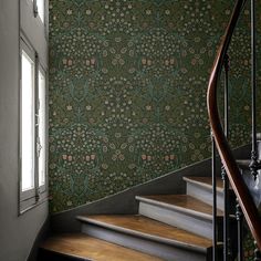 a stair case with floral wallpaper and wooden handrails next to a window