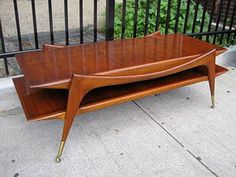 a wooden coffee table sitting on top of a sidewalk next to a metal fence and black iron railing