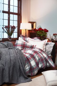 a bed with plaid comforter and pillows in a room next to a table with flowers