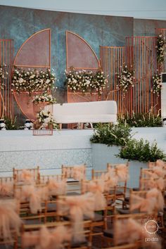 an outdoor ceremony setup with chairs and flowers on the back wall, surrounded by greenery