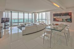 a living room filled with white furniture next to tall windows and a large painting on the wall