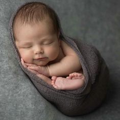 a newborn baby is curled up and sleeping on a gray blanket with his hands under his chin