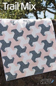 a pink and black quilt sitting on top of a stone wall next to a tree