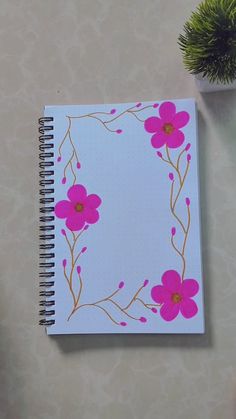 a notebook with pink flowers on it next to a potted plant