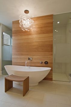 a large white bath tub sitting next to a wooden wall in a bathroom under a chandelier