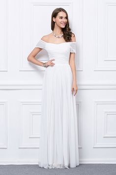 a woman standing in front of a white wall wearing a dress with an off the shoulder neckline