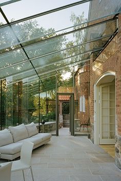 a living room filled with white furniture under a glass covered roof over an outdoor patio