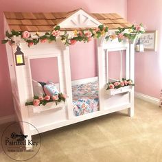 a child's bed made out of white wood with pink flowers on the roof