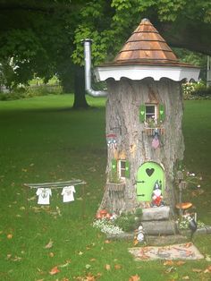 a tree stump with a green door and window on it in the middle of a park