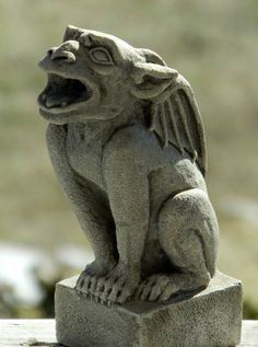 a gargoyle statue sitting on top of a cement block with its mouth open